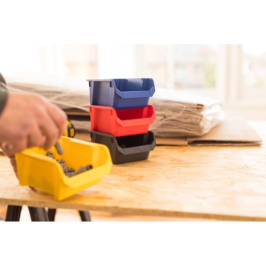 STANLEY STST82737-1 bacs de rangement empilables en plastique bleu, rouge, noir et jaune sur une table d’atelier.