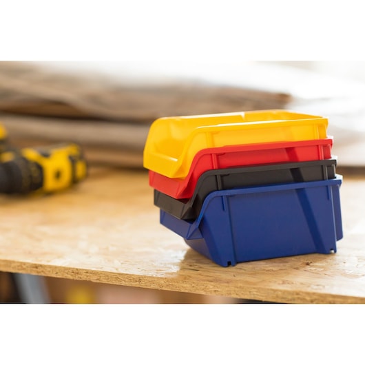 STANLEY STST82740-1 stapelbare plastic bakken in geel, rood, zwart, blauw op een werkbank, zijaanzicht.
