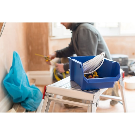 STANLEY STST82743-1 bac de rangement bleu avec câbles et outils sur un escabeau dans un espace de travail.