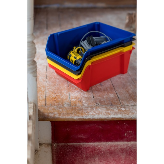 STANLEY STST82745-1 bacs de rangement empilables rouges, jaunes et bleus avec outils sur plancher en bois.
