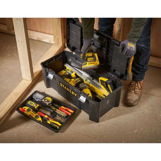 Boîte à outils STANLEY STST82976-1 remplie d’outils à main et électriques, ouverte sur le sol de l’atelier, vue de dessus en angle.