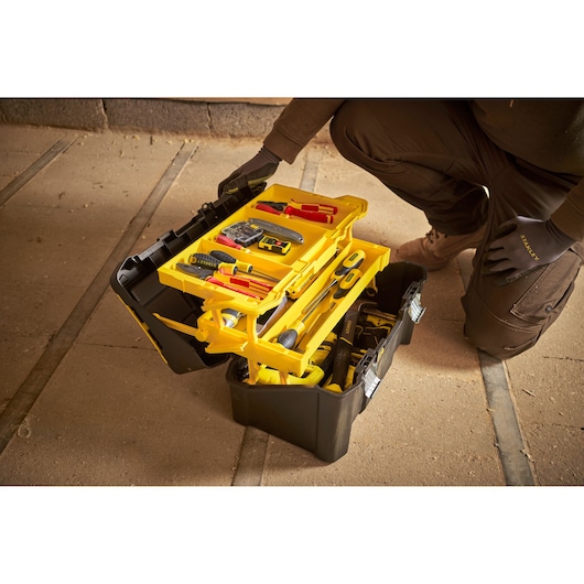 STANLEY STST83397-1 zwarte en gele gereedschapskist met open trays en handgereedschap op werkplaatsvloer.