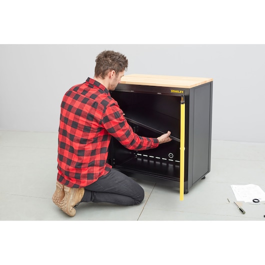 STANLEY STST97595-1 fotografie van persoon die een zwarte kast met houten blad monteert, instructies erbij.
