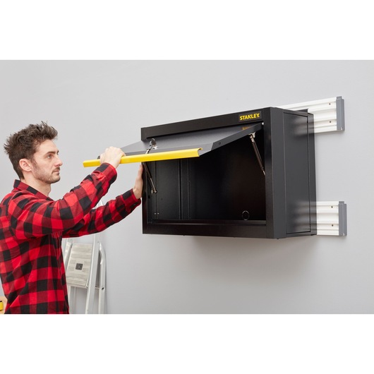 Stanley STST97599-1 armoire murale de rangement avec poignée jaune, ouverte par une personne, environnement garage.