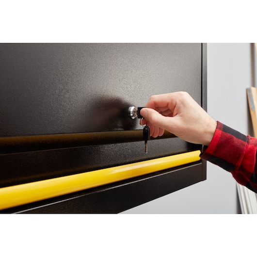 STANLEY STST97599-1 boîte à outils noire vue de face, main tournant la clé dans la serrure, poignée jaune.