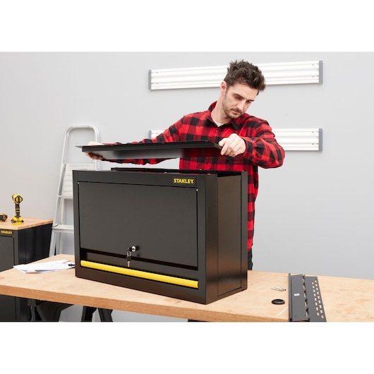 STANLEY STST97599-1 armoire à outils noire en acier avec poignée jaune, personne en cours de montage sur établi.