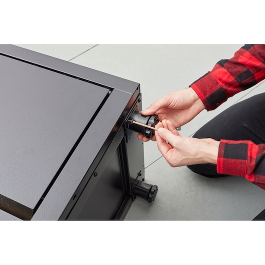STANLEY STST97957-1 photographie d’une personne assemblant une roulette sur armoire métallique noire.