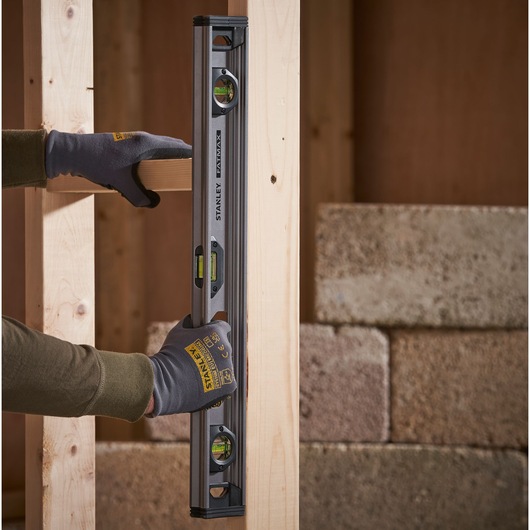 Foto van STANLEY XTHT1-42131 waterpas verticaal op houten frame, vastgehouden met handschoenen.